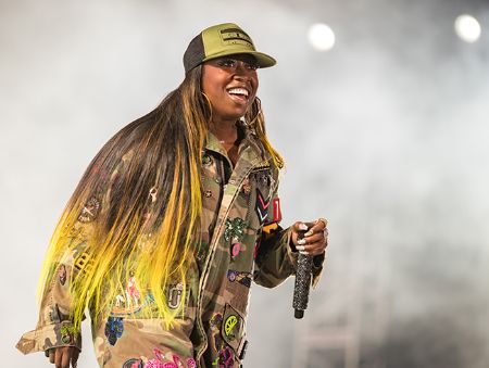 Missy Elliott in a grey top and a cap at a concert.